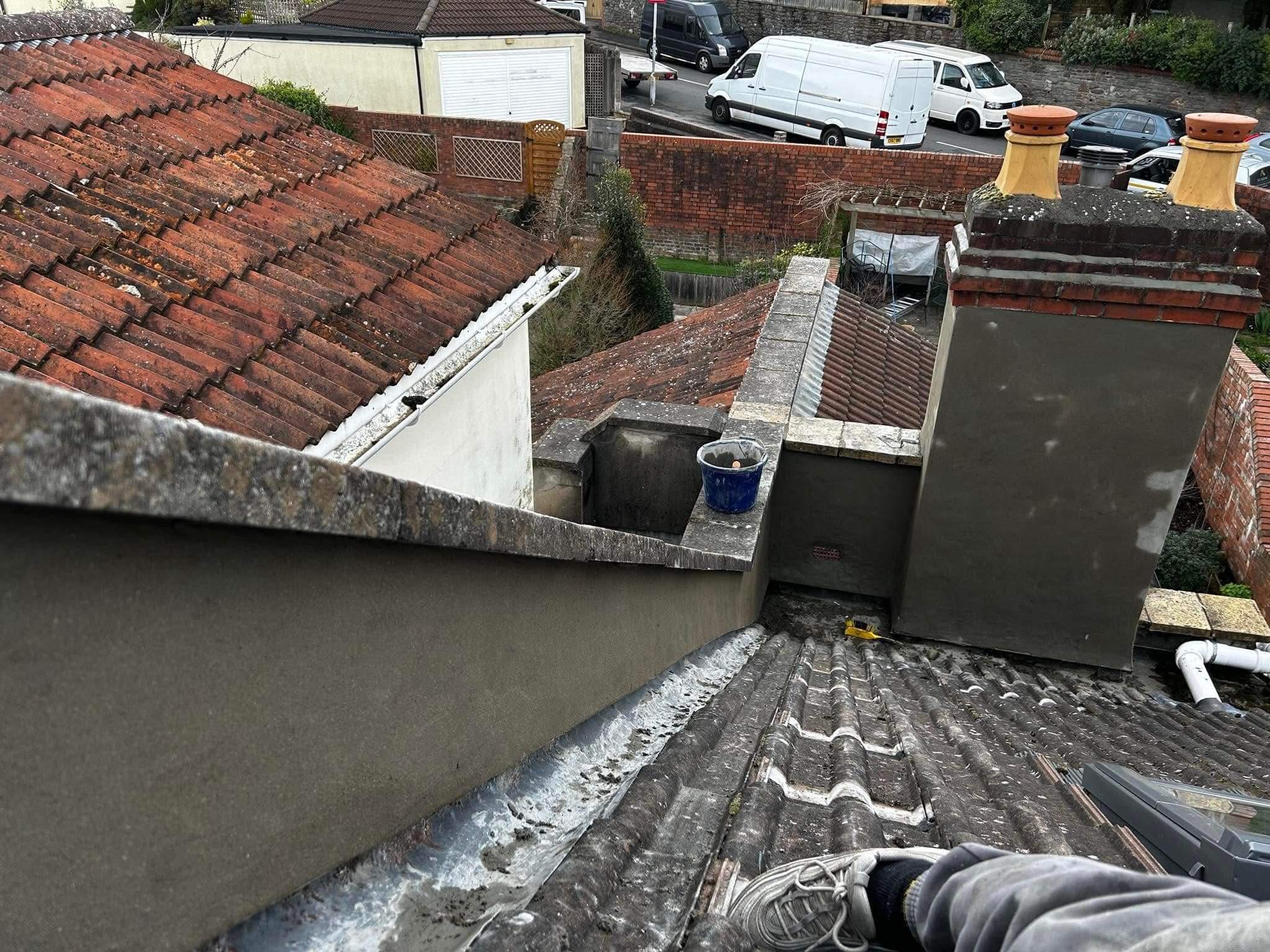 View from a rooftop showing a brick chimney with dual yellow chimney pots, surrounding tiled roofs, and a parked white van on the street below.
