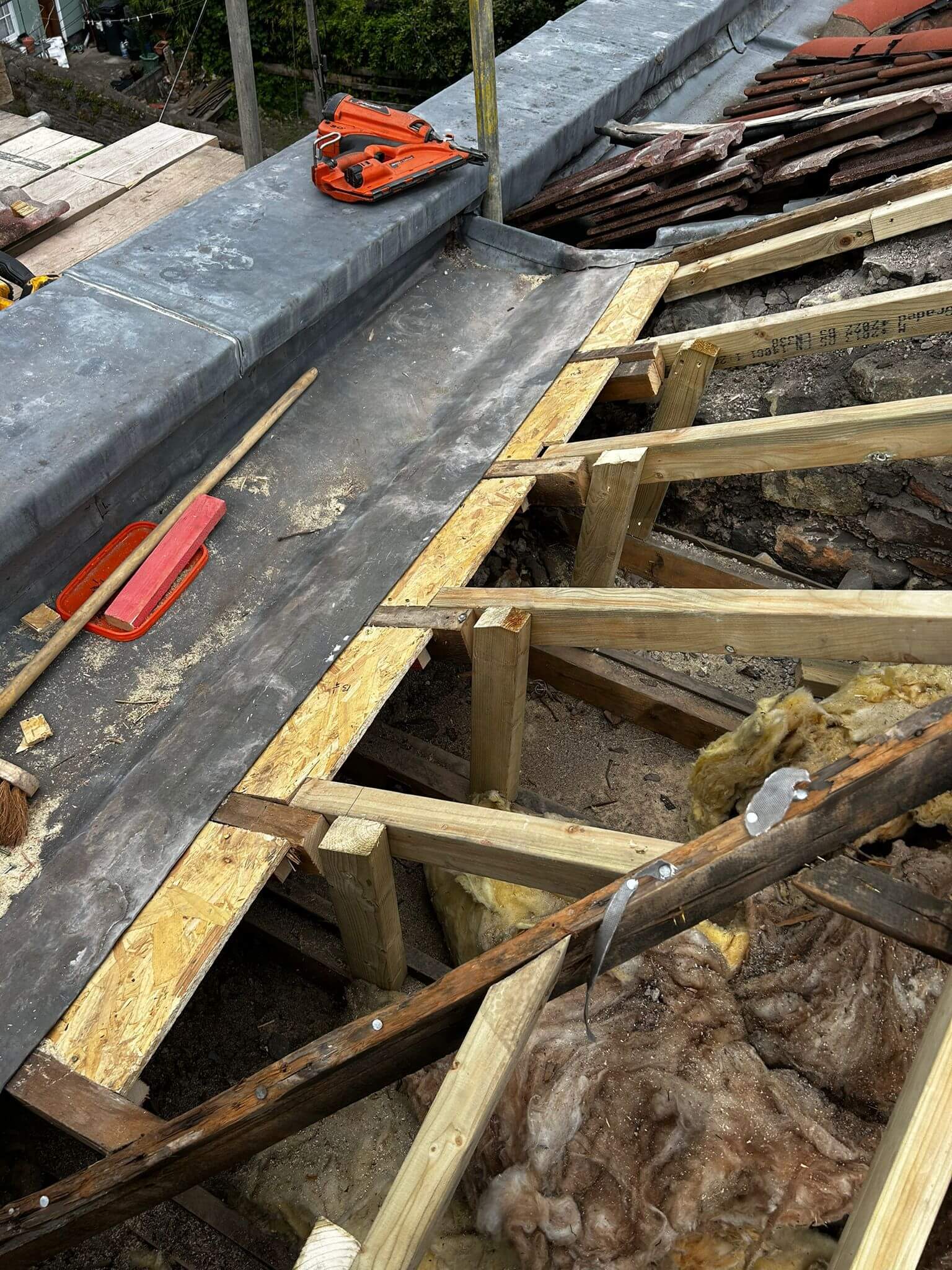 Partially constructed roof with exposed wooden beams, insulation, and roofing materials visible, along with tools and debris on the surface.