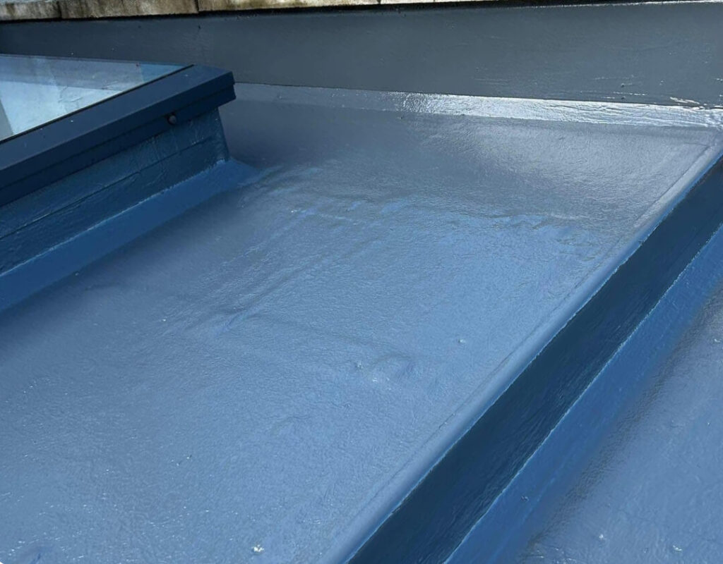 A close-up view of a flat roof with a smooth blue waterproof coating, featuring slight surface ripples beside a raised edge and window frame—ideal for projects that repair fascia and soffit.